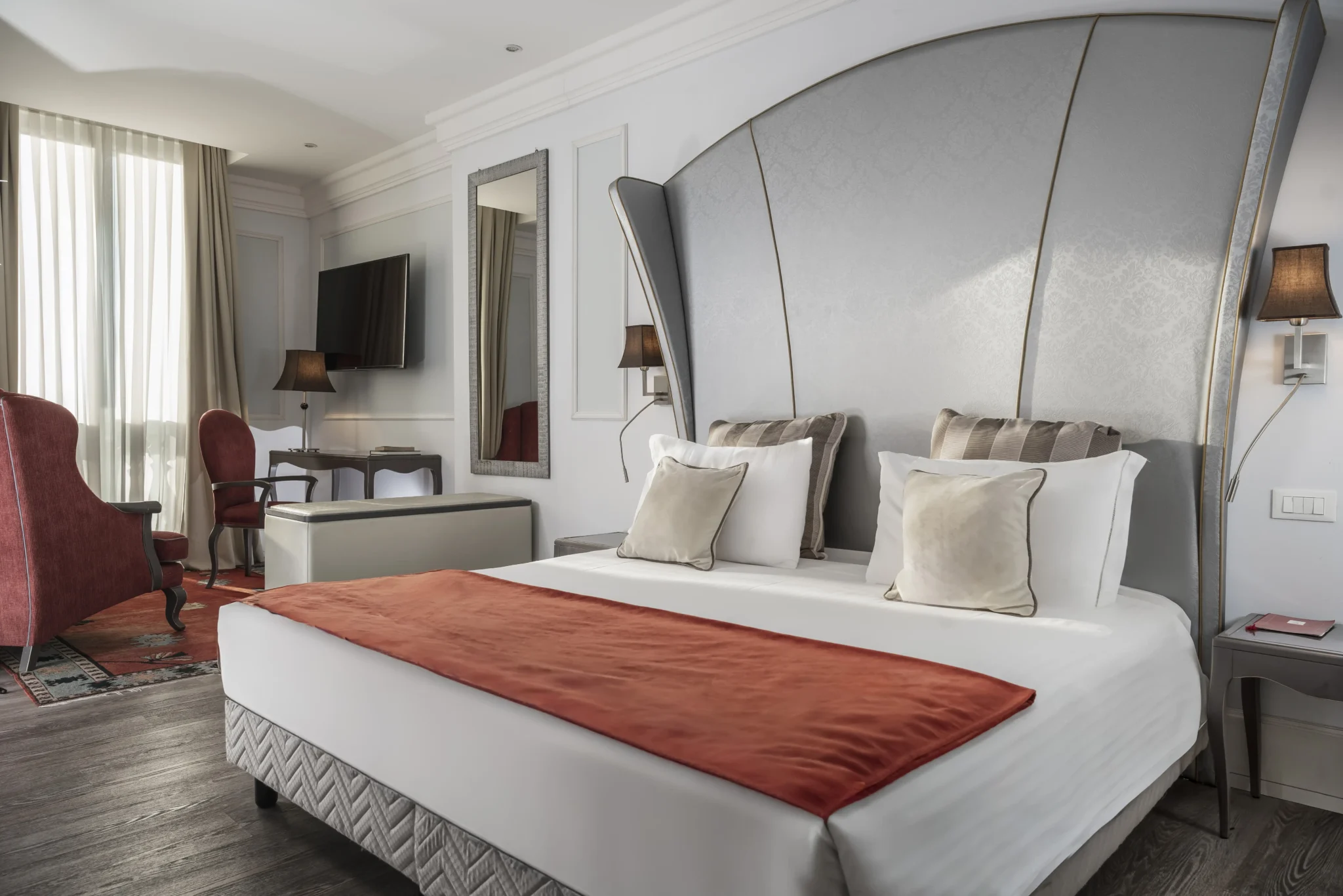 Camera da letto elegante con letto matrimoniale, testiera grigia e poltrone rosse.