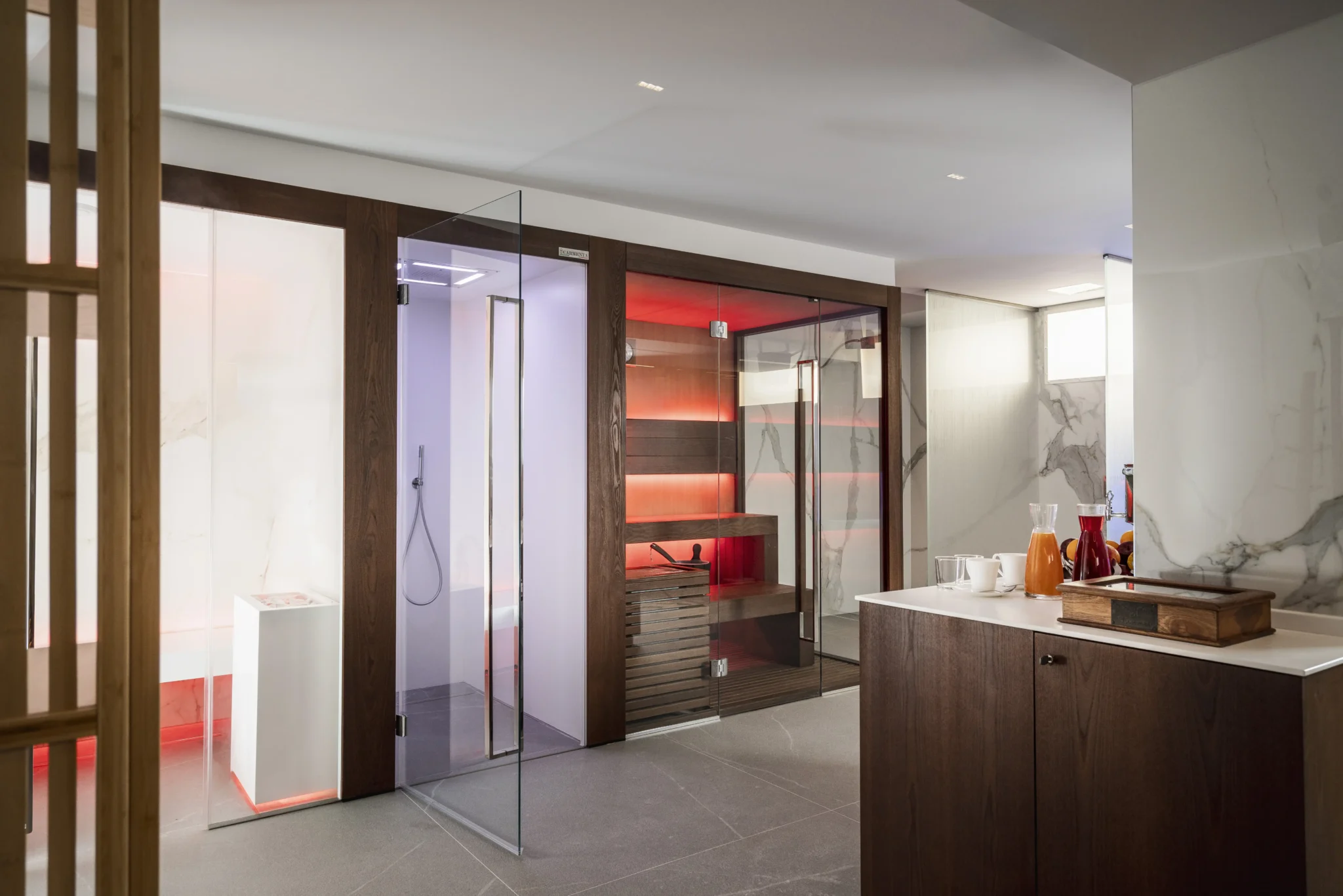 Sala spa moderna con sauna e doccia in vetro, illuminata da luci colorate.