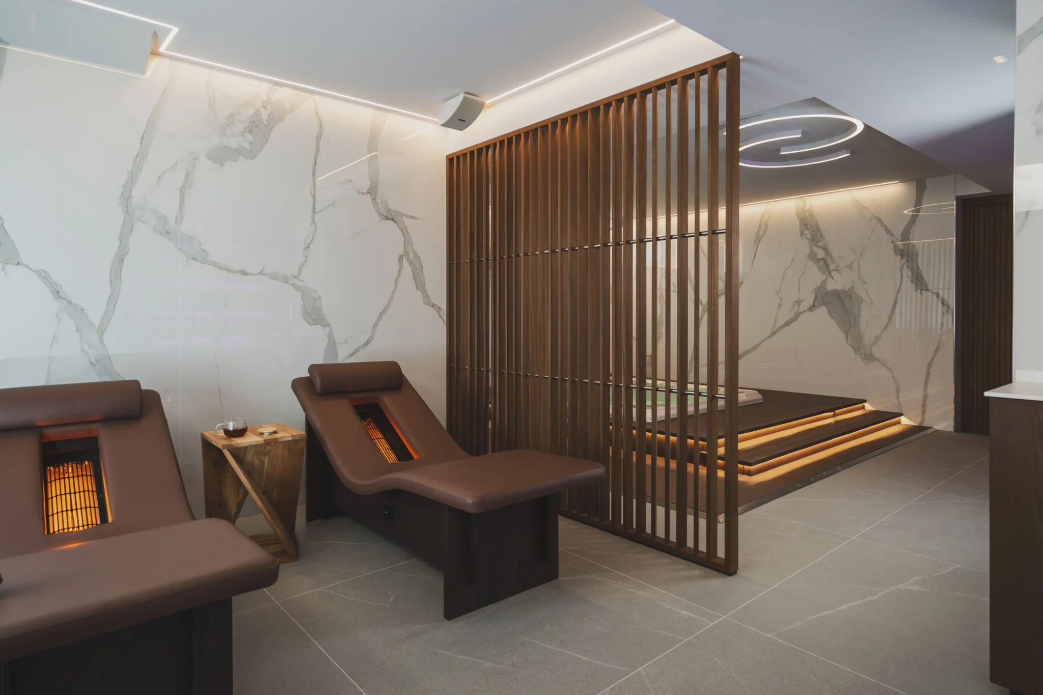 Sala relax moderna con poltrone riscaldate, pareti di marmo e illuminazione soffusa.