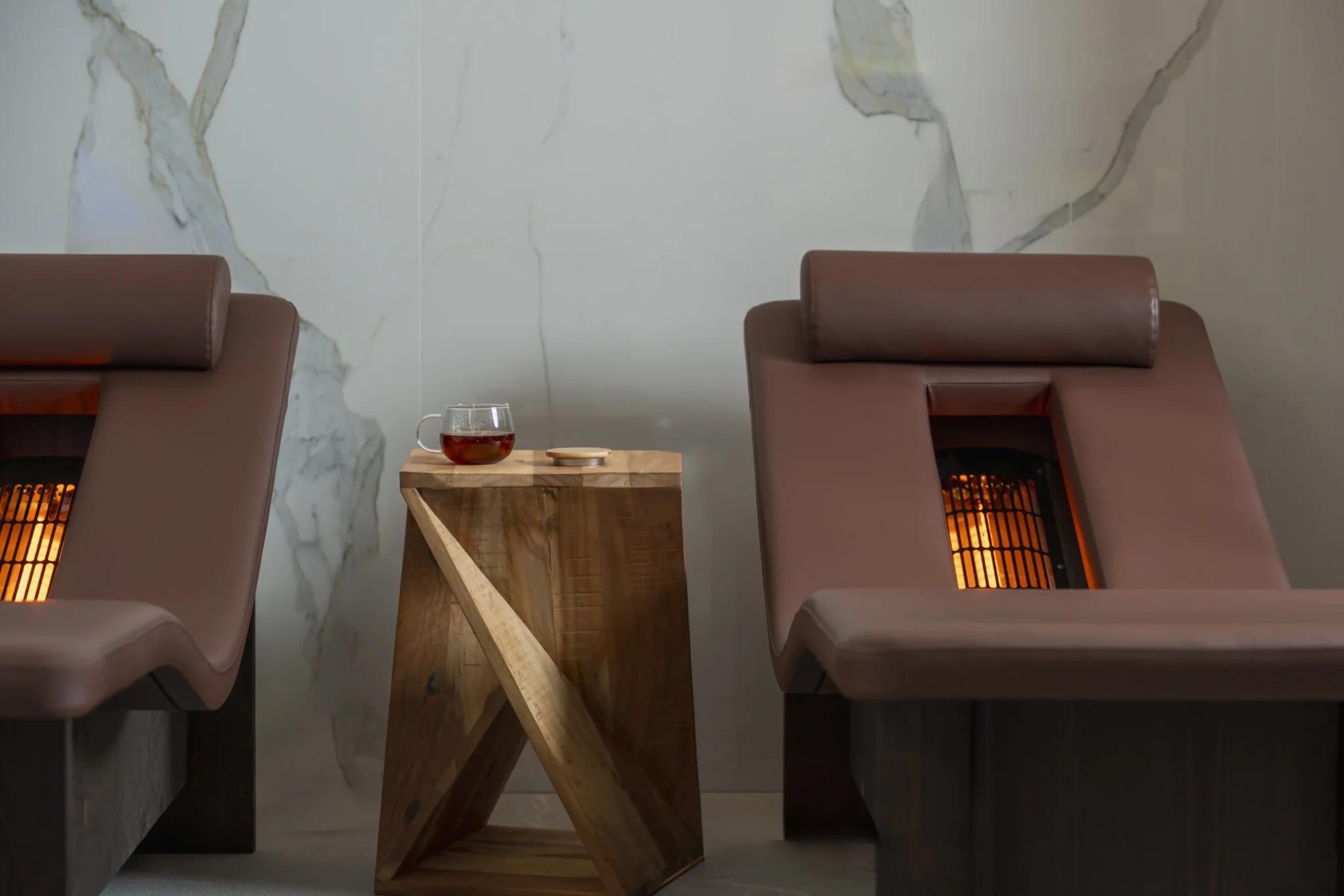 Due chaise longue marroni con riscaldamento integrato affiancano un tavolino in legno con una tazza di t&egrave; sopra.