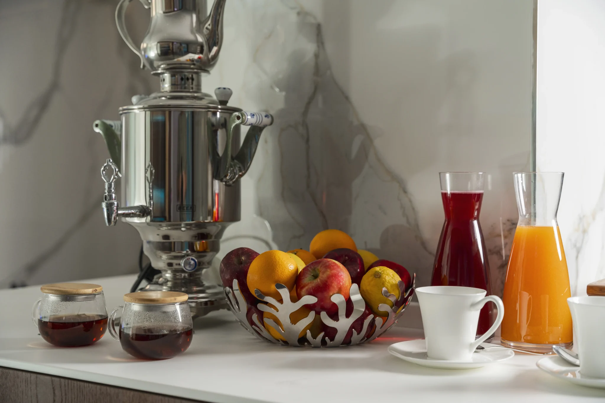 Samovar d'acciaio con frutta fresca e caraffe di succhi su un piano di cucina.