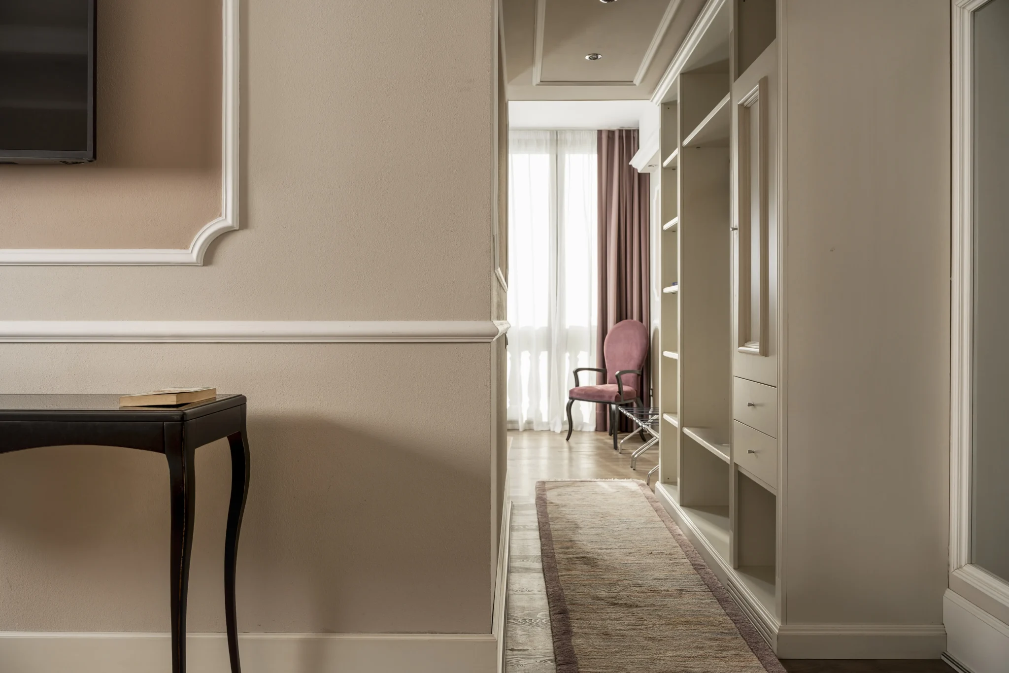 Interno elegante con corridoio, tavolino nero e sedia rosa.
