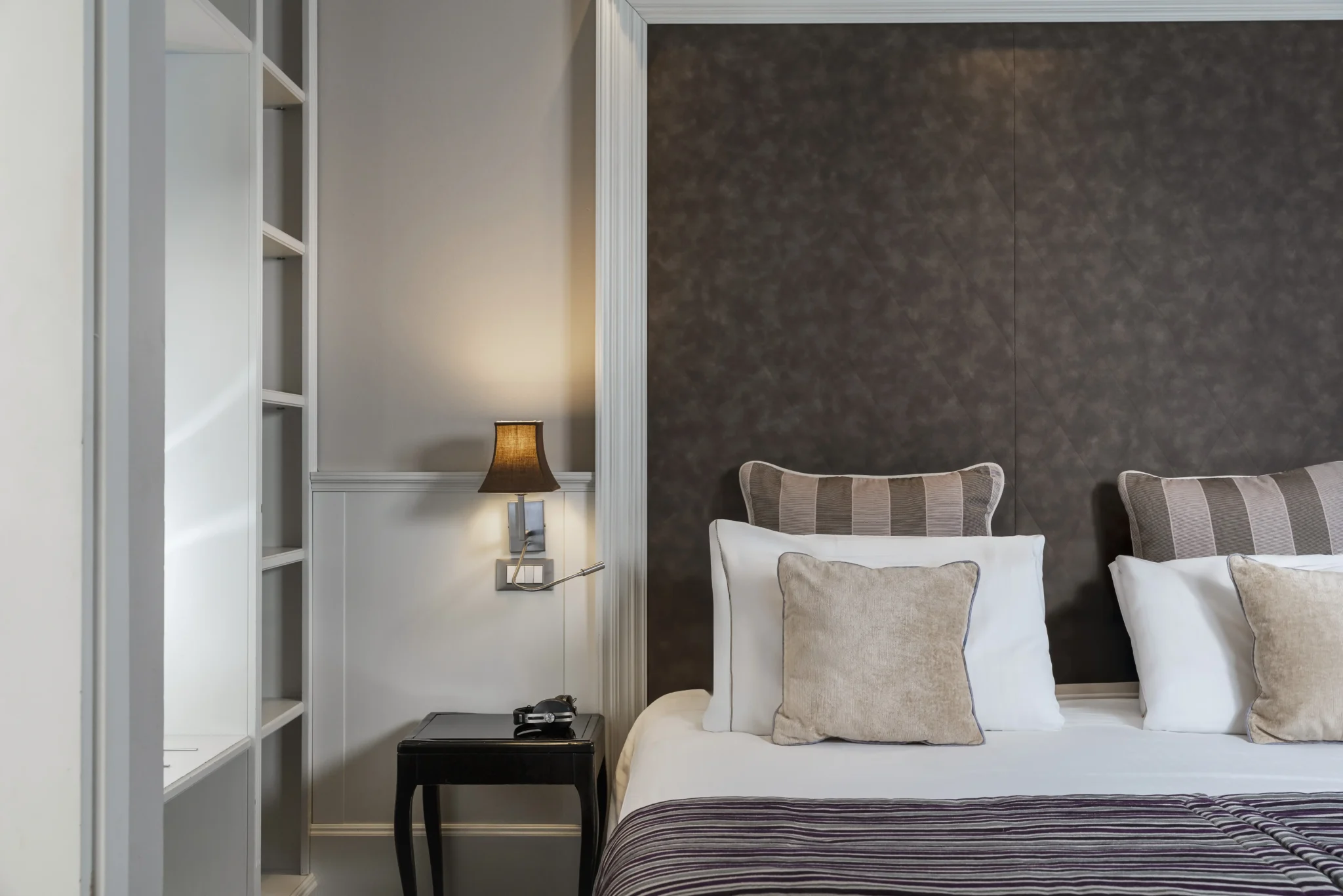 Camera da letto elegante con letto matrimoniale, cuscini decorativi e lampada da parete.