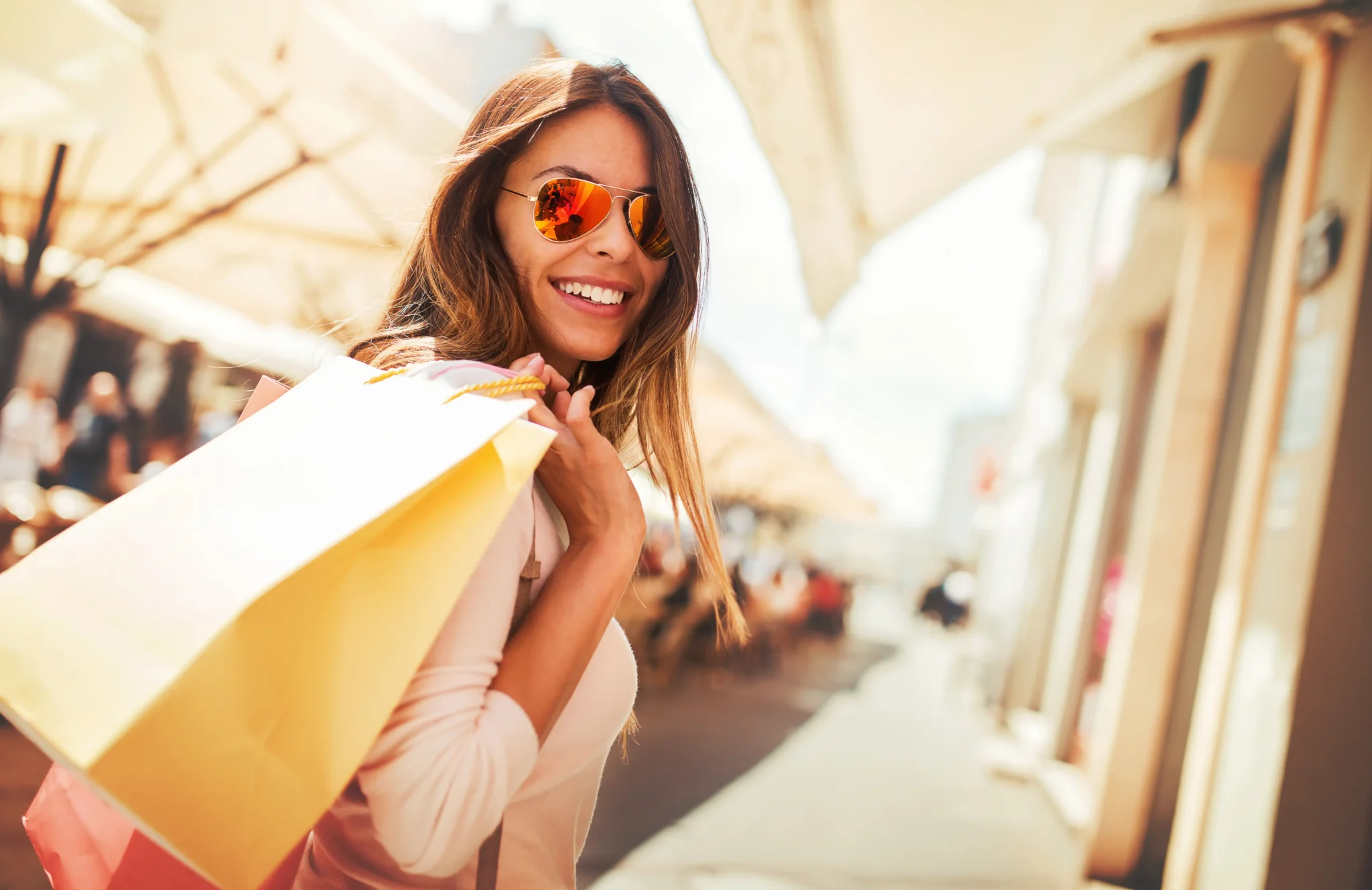 Donna sorridente con occhiali da sole e borse da shopping in strada.